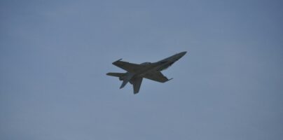 Military fighter jet flying overhead against a clear blue sky, symbolizing American air power and defense readiness.